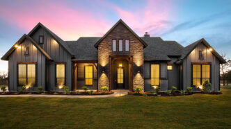 Two-story upper middle class contemporary suburban home emblazoned with landscape lighting, including multi-directional sconce lights, accent lights, path lights, and wall wash lights.
