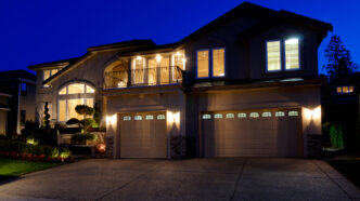Front view of upper middle class two-car-garage home with accent lights and path lights welcoming visitors.