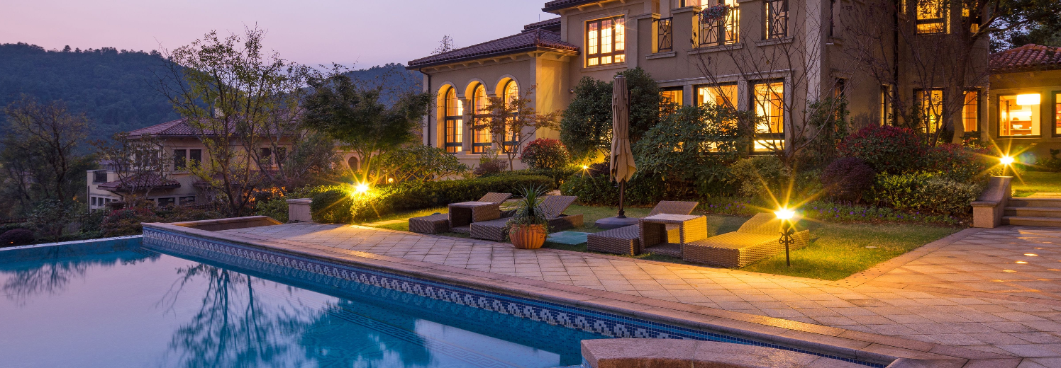 Backyard of an opulent home with a swimming pool, accent lights, path lights.