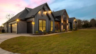 Angled view of upper middle class farm house with outdoor lighting at dusk.