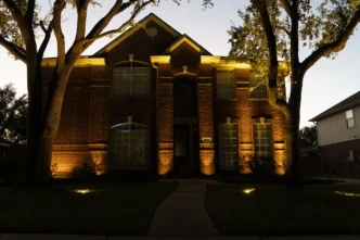 Uplights and inground well lights illuminating an upper middle class brick house at dusk.