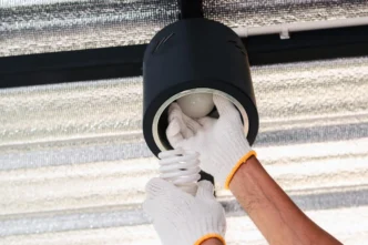 Person using gloves to remove a broken light bulb from a downlighting fixture.