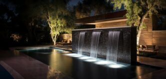 Outdoor home modern water feature fountain waterfall on swimming pool with underwater dramatic lighting.