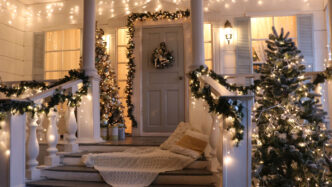 A front porch adorned with white exterior Christmas lights, garland, Christmas wreath, and other holiday decor.