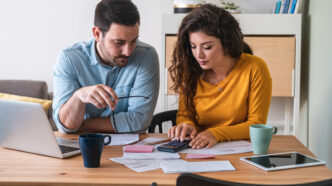 Young couple analyzing their bills to budget expenses strewn out in front of them at a table with a laptop.