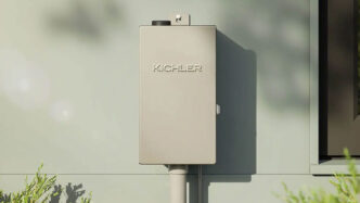 Stainless steel Kichler lighting transformer attached to the side of a house.