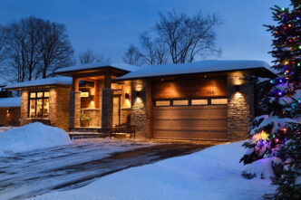 Snow covered modern house in with outdoor and winter lighting around Christmastime.