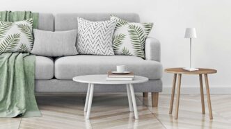 Portable white Zafferano Poldina Pro lamp resting on a stool next to a couch and coffee table.