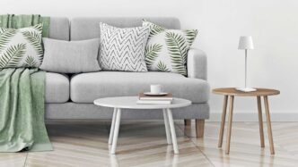 Portable white Zafferano Poldina Pro lamp resting on a stool next to a couch and coffee table.