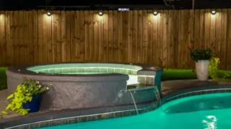 A backyard swimming pool and jacuzzi hot tob at night with solar lights around the fence for privacy and illumination.