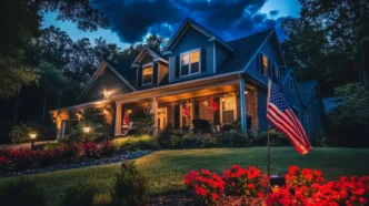 American flag illuminated by uplights in a red flower garden in the foreground of a comfortable middle class home.