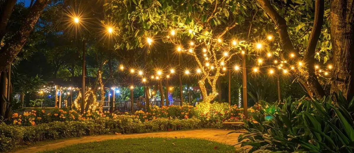 Bistro string lights woven throughout a tree adjacent to an open patch of grass encircled by a brick walkway.