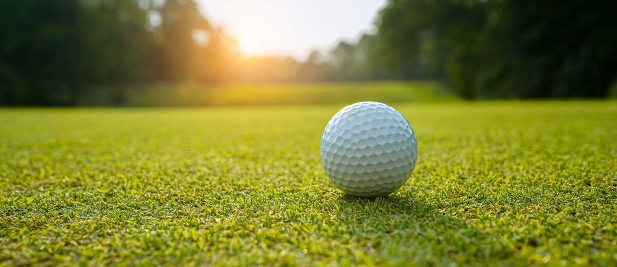 Golf ball on a golf course green with sunsetting in the background.