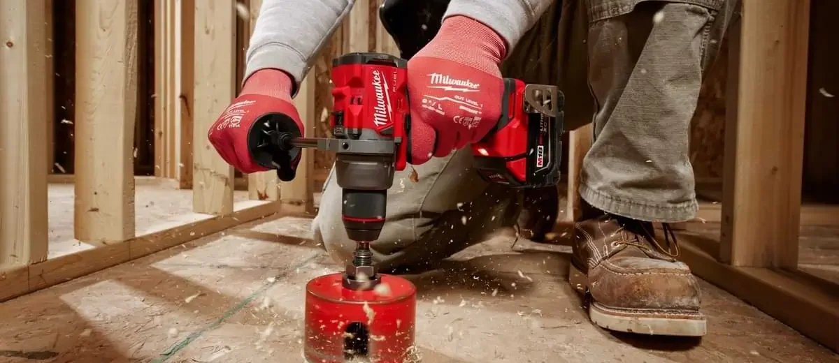 Person using Milwaukee Tool driver to drill through plywood with a construction scene backdrop.