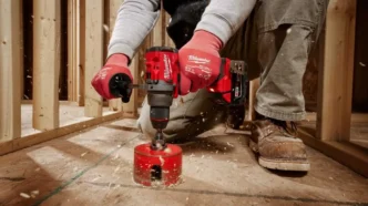 Person using Milwaukee Tool driver to drill through plywood with a construction scene backdrop.