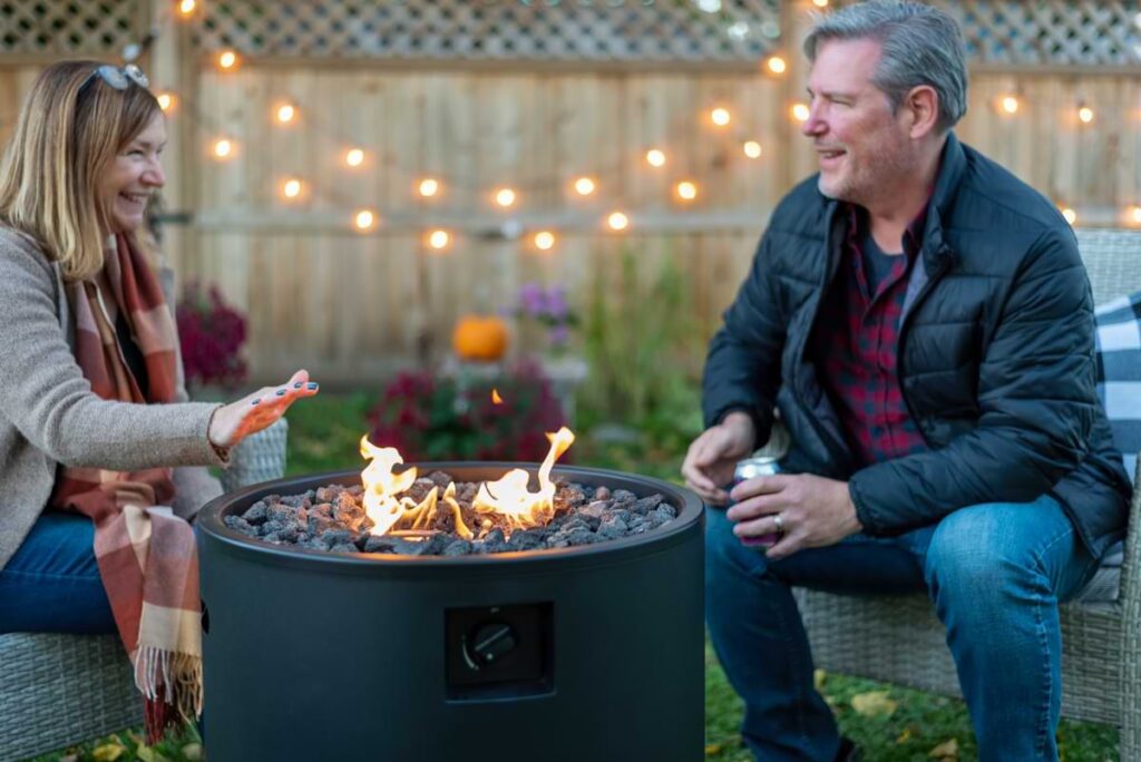 Middle aged couple sitting around a round aluminum firepit at dusk.