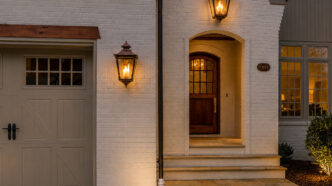 Front of white brick home with two outdoor coach lights, one above the doorway arch and one to the right of the garage door.